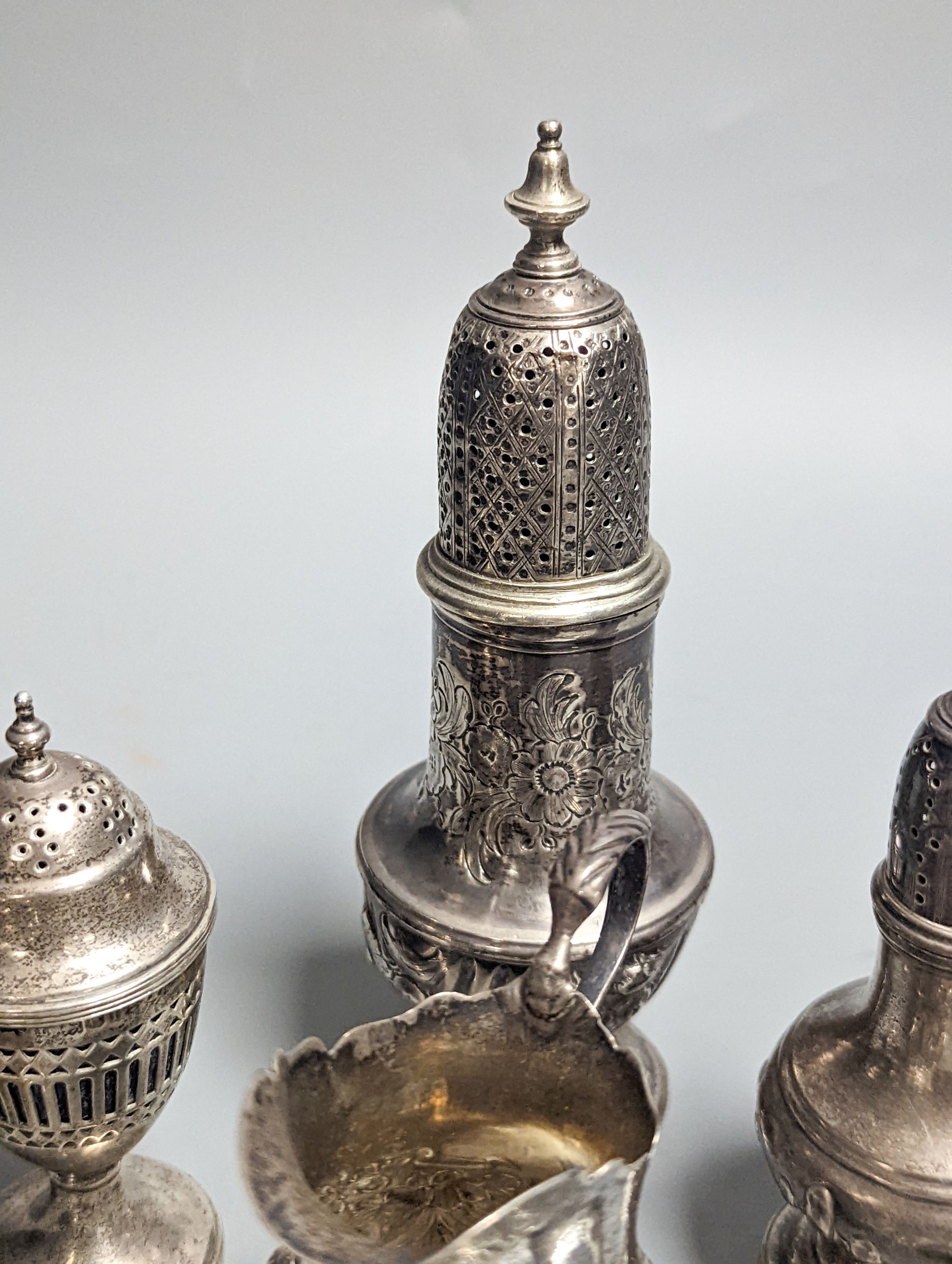 A Victorian embossed silver cream jug, London, 1883, 92mm, two 18th century silver pepperettes, one with plated cover, four later condiments (two silver), a silver spoon and small 800 standard photograph frame.